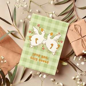 printable silly goose card. soft gingham background with two geese lying on their backs surrounded by flowers. text reads love you silly goose. Printable anniversary card for boyfriend or girlfriend