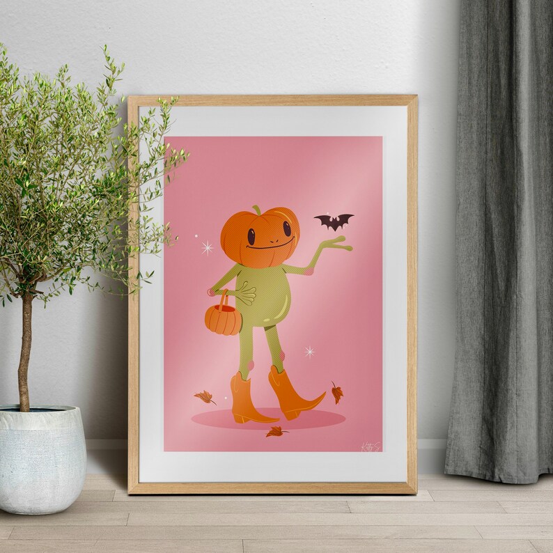 howdy halloween frog art print in pink, green and orange in wooden frame. UPS style cartoon illustration of a frog with a pumpkin head wearing orange cowboy boots and carrying a pumpkin bag. next to him flies a little bat, leaves surround his feet