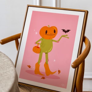 howdy halloween frog art print in pink, green and orange in wooden frame. UPS style cartoon illustration of a frog with a pumpkin head wearing orange cowboy boots and carrying a pumpkin bag. next to him flies a little bat, leaves surround his feet