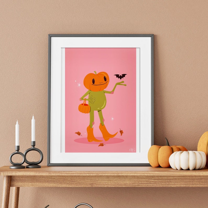 halloween frog art print in pink, green and orange surrounded by pumpkins. UPS style cartoon illustration of a frog with a pumpkin head wearing orange cowboy boots and carrying a pumpkin bag. next to him flies a little bat, leaves surround his feet