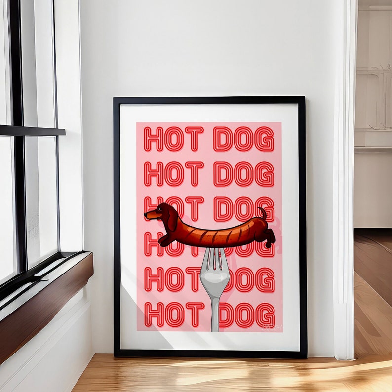 Printable pink & red dog art print. Soft pink background with red text in the style of neon lights reading HOT DOG. in the centre of the art print is a dachshund in the shape of a sausage on the end of a silver fork in a playful style in black frame