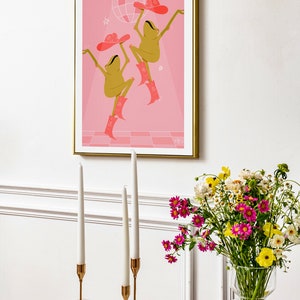 aesthetic dining room with wildflowers and tall candles. On the wall is a pink frog art print of two frogs dancing beneath a sparkling disco ball