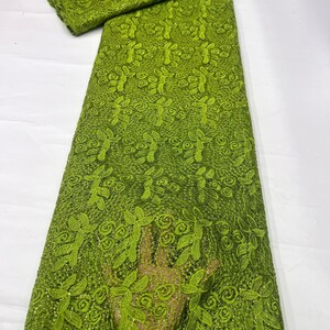 May include: A vibrant lime green lace fabric featuring an intricate embroidered pattern of swirling floral motifs and leaves. The textile has a delicate mesh base with a subtle shimmering finish throughout, showcasing a repeating botanical design.