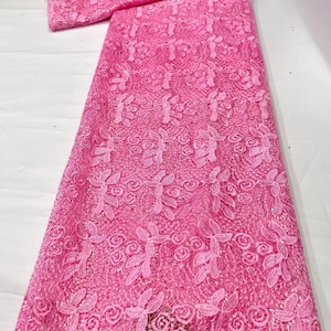 May include: A vibrant pink lace fabric featuring an intricate floral pattern with embroidered leaves and rose-like blossoms. The textile is embellished with small, shimmering sequins throughout the mesh base, creating a textured and reflective surface.