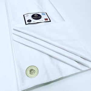 May include: Folded white fabric with a delicate geometric design. The fabric features a label stating "SUPER ATIKU SWISS VOILE". A gold seal with a lion emblem is also present. The fabric is likely of high quality, suitable for garments or textile projects.