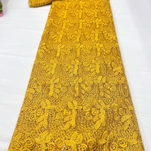 May include: A vibrant mustard yellow lace fabric featuring an intricate floral pattern with embroidered leaves and swirling rose-like motifs. The textile is embellished with small, shimmering sequins throughout the mesh base, creating a textured appearance.