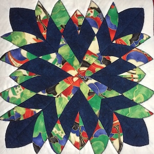 May include: A blue and green patchwork quilt block with a starburst design. The block is made of various fabrics with floral and geometric patterns.