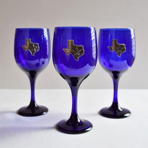 May include: Three cobalt blue wine glasses with silver Texas state outlines and a star on each.