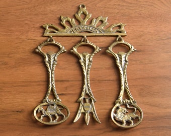 May include: Three gold-toned metal spoons with decorative designs hang from a metal crown-shaped piece with the word "Jerusalem" inscribed on it.