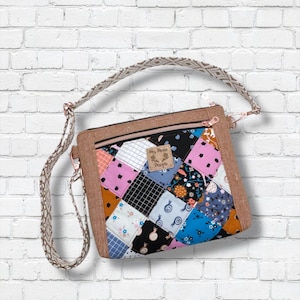 May include: A patchwork crossbody bag with a brown frame and a patterned strap. The bag features a variety of colorful fabric squares in pink, blue, black, and white. The bag has a zipper closure and a small label that reads "My Moose Designs."