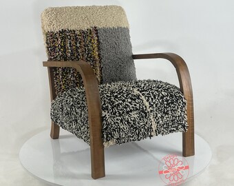 May include: A brown wooden armchair with a black and white patterned tufted cushion. The cushion is made of a thick, fuzzy fabric. The chair has a curved back and arms.