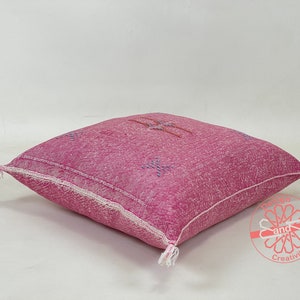 May include: A pink and white patterned floor cushion with a fringe detail. The cushion is made of a soft, woven fabric and has a subtle sheen.