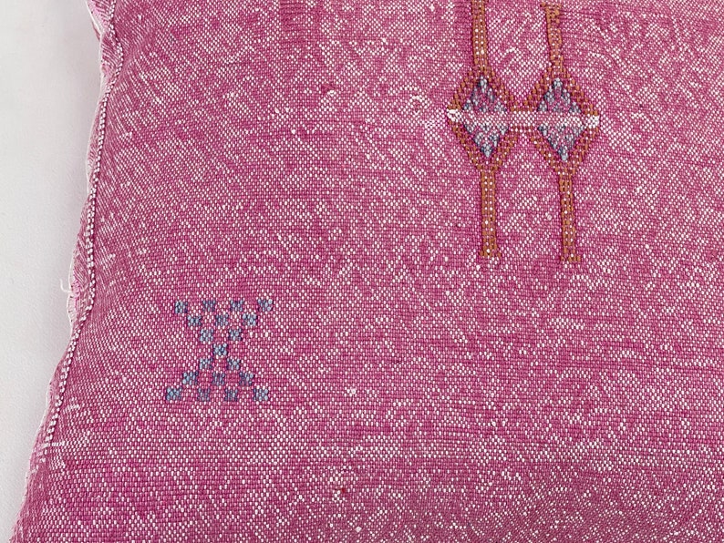 May include: Pink throw pillow with a woven design featuring geometric shapes in brown and gray.