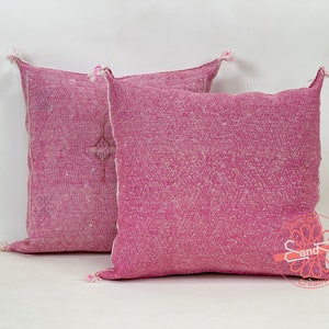May include: Two pink throw pillows with a subtle woven pattern and fringe detailing. The pillows are made of a soft, textured fabric.