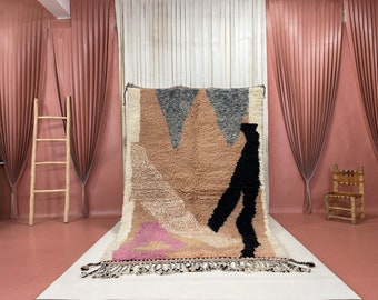 May include: A large, abstract rug with geometric shapes in shades of brown, pink, white, and black. The rug has a fringe border and is displayed on a white surface.