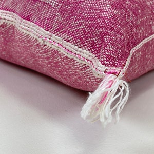 May include: Close-up of a pink and white throw pillow with a white tassel. The pillow is made of a soft, textured fabric.