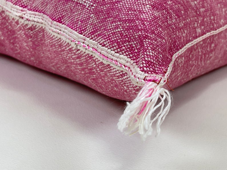 May include: Close-up of a pink and white throw pillow with a white tassel. The pillow is made of a soft, textured fabric.