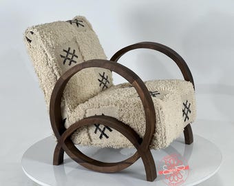 Puede incluir: Un sillón blanco con un marco de madera marrón. El sillón tiene una tapicería de tela blanca y mullida con un patrón geométrico negro. El sillón está sobre un pedestal blanco.