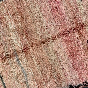 Op de afbeelding: Een close-up van een roze en beige Marokkaans tapijt met een geweven patroon. Het tapijt heeft een zachte, pluche textuur.