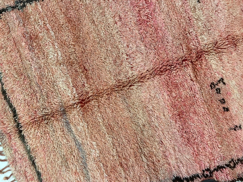 Op de afbeelding: Een close-up van een roze en beige Marokkaans tapijt met een geweven patroon. Het tapijt heeft een zachte, pluche textuur.