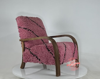 May include: A pink armchair with black patterned upholstery and wooden arms. The chair is on a white pedestal.