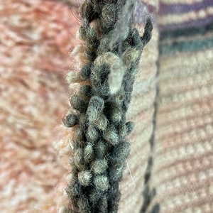 Op de afbeelding: Close-up van een dik, donkergrijs garen met witte, pluizige vezels die er doorheen geweven zijn. Het garen is getextureerd en heeft een pluche uitstraling.
