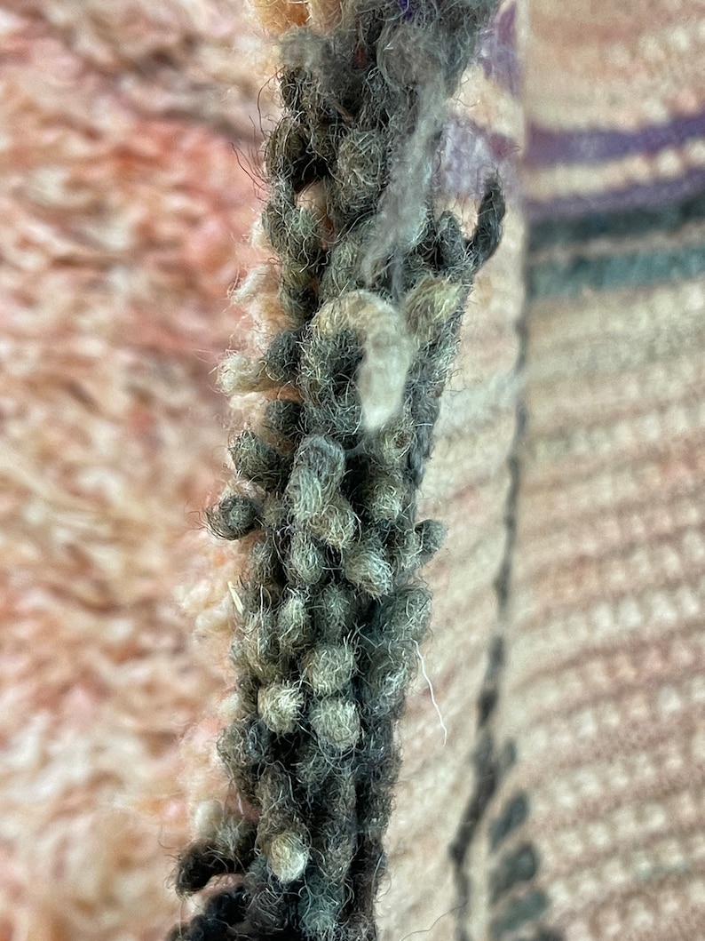 Op de afbeelding: Close-up van een dik, donkergrijs garen met witte, pluizige vezels die er doorheen geweven zijn. Het garen is getextureerd en heeft een pluche uitstraling.