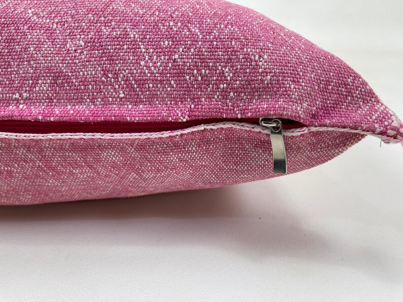 May include: A pink pillow with a white zipper. The pillow is made of a textured fabric.