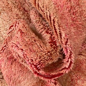 Op de afbeelding: Close-up van een zachte, roze en rode, pluche stof met een textuur, geweven patroon.