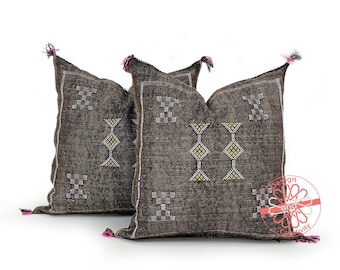 May include: Two brown throw pillows with geometric patterns and tassels. The pillows have a dark brown background with white and gold embroidery.