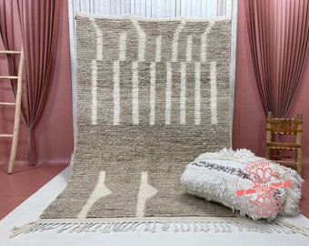 May include: A beige and white Moroccan rug with a geometric pattern. The rug has a fringe border and is made of wool.