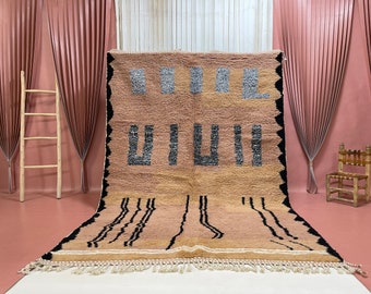 May include: A large, rectangular rug with a geometric pattern in shades of brown, black, and white. The rug has a fringe border and is made of wool.