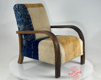 May include: A wooden armchair with curved arms and a patterned fabric upholstery in shades of blue, beige, and brown. The chair is on a white pedestal.