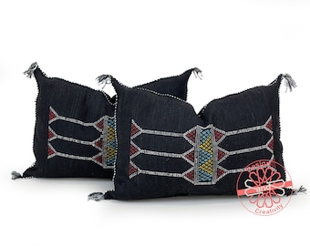 May include: Two black throw pillows with embroidered geometric patterns in white, red, blue, and yellow. The pillows have tassels on the corners.