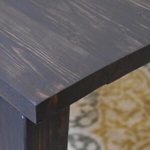 May include: Close-up of a dark stained wooden table top with visible wood grain. The table has a square top and a single leg visible in the image.