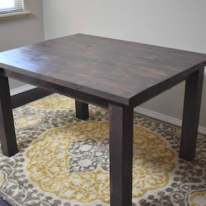 May include: A dark brown wooden table with a rectangular top and four legs. The table is sitting on a rug with a floral pattern.