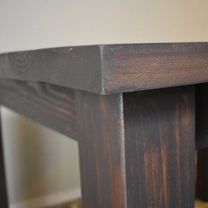 May include: Close-up of a dark stained wooden table with a simple design. The table has a rectangular top and four legs.