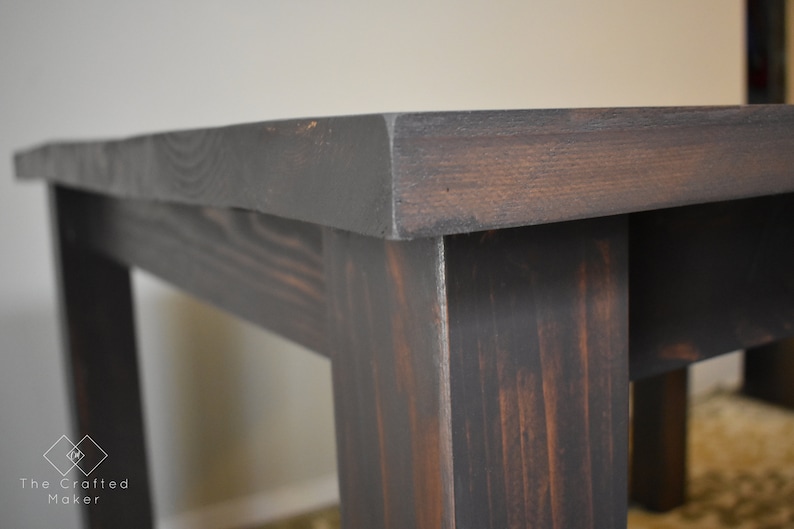 May include: Close-up of a dark stained wooden table with a simple design. The table has a rectangular top and four legs.