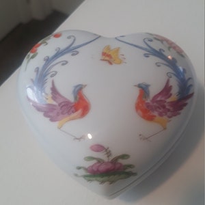 Könnte beinhalten: Weiße Porzellan-Schmuckschatulle in Herzform mit einem bemalten Design aus zwei bunten Vögeln mit langen Schwänzen, einem Schmetterling und floralen Akzenten.
