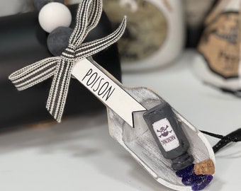 May include: A white wooden scoop with a black and white striped ribbon tied around it. The scoop has a small black bottle with a skull and crossbones and the word "ARSENIC" on it. The scoop also has a white tag with the word "POISON" written on it.