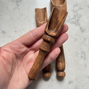 May include: Three wooden spoons with a dark brown stain. The spoons have a rounded scoop at the end and a long handle.