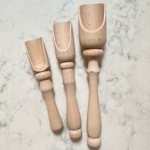 May include: Three wooden scoops of varying sizes, all with a natural wood finish and rounded handles. The scoops are arranged in a row on a white marble surface.