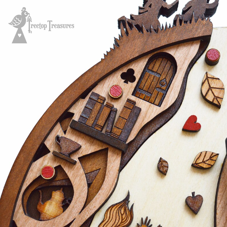 K&ouml;nnte beinhalten: Mehrschichtiges Holzkunstwerk mit einer fantastischen Szene mit einer T&uuml;r, B&uuml;chern und fallenden Bl&auml;ttern. Das Kunstwerk enth&auml;lt eine Teetasse, eine Teekanne und ein herzf&ouml;rmiges Element. Das Kunstwerk besteht aus verschiedenen Braunt&ouml;nen und tr&auml;gt den Text "Treetop Treasures".