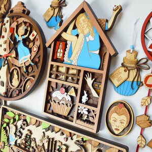 K&ouml;nnte beinhalten: Eine Sammlung von Holzdekorationen mit Laserschnitt, die Charaktere und Szenen aus Alice im Wunderland zeigen. Enth&auml;lt eine Uhr, ein Haus, eine Flaschen- und Spielkarten-Designs. Die Farbpalette umfasst Braun-, Blau-, Rot- und Wei&szlig;t&ouml;ne.