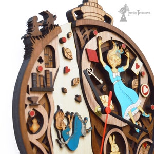 K&ouml;nnte beinhalten: Holzuhr mit einem mehrschichtigen Design zum Thema Alice im Wunderland. Das Zifferblatt zeigt Alice beim Fallen, Spielkarten und ein wei&szlig;es Kaninchen. Die Zeiger der Uhr sind rot, und der Rahmen besteht aus verschiedenen Braunt&ouml;nen.