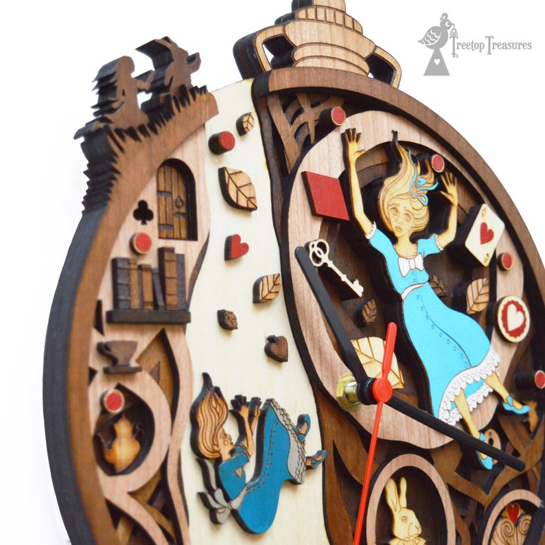 K&ouml;nnte beinhalten: Holzuhr mit einem mehrschichtigen Design zum Thema Alice im Wunderland. Das Zifferblatt zeigt Alice beim Fallen, Spielkarten und ein wei&szlig;es Kaninchen. Die Zeiger der Uhr sind rot, und der Rahmen besteht aus verschiedenen Braunt&ouml;nen.