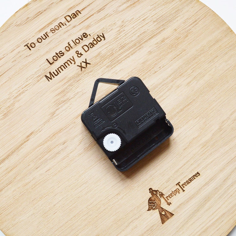May include: A wooden clock face with a personalized message: "To our son, Dan Lots of love, Mummy & Daddy XX". The clock face is attached to a black clock mechanism with a white knob.