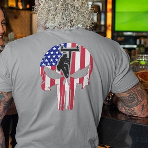 May include: A gray t-shirt with a graphic of a skull with the American flag design. The skull has a silhouette of a lineman working on a power line.