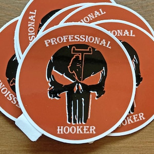 Pode incluir: Um conjunto de cinco adesivos redondos laranja com texto branco e um gráfico de caveira preta. O texto do adesivo diz "Professional Hooker".