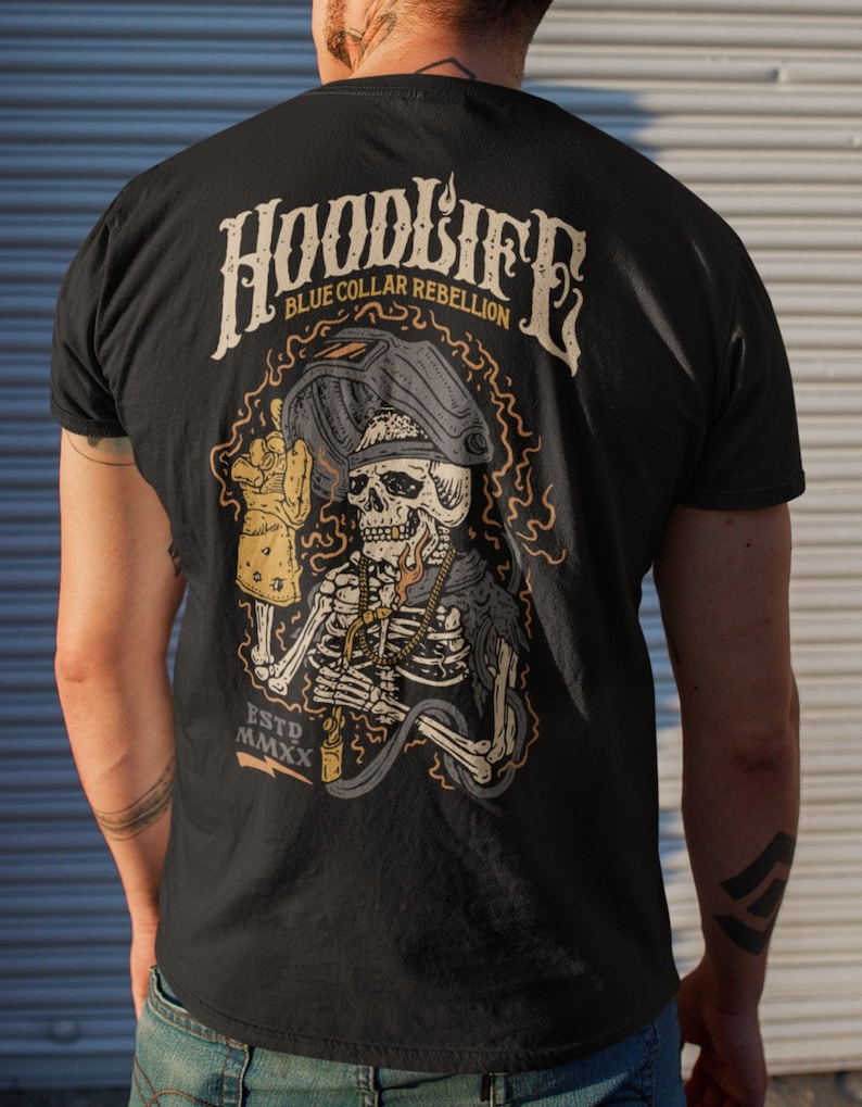 Pode incluir: Camiseta preta com um gr&aacute;fico de um esqueleto usando uma m&aacute;scara de solda e segurando um ma&ccedil;arico de solda. O texto "HOODLIFE BLUE COLLAR REBELLION ESTD MMXX" est&aacute; impresso na camiseta.